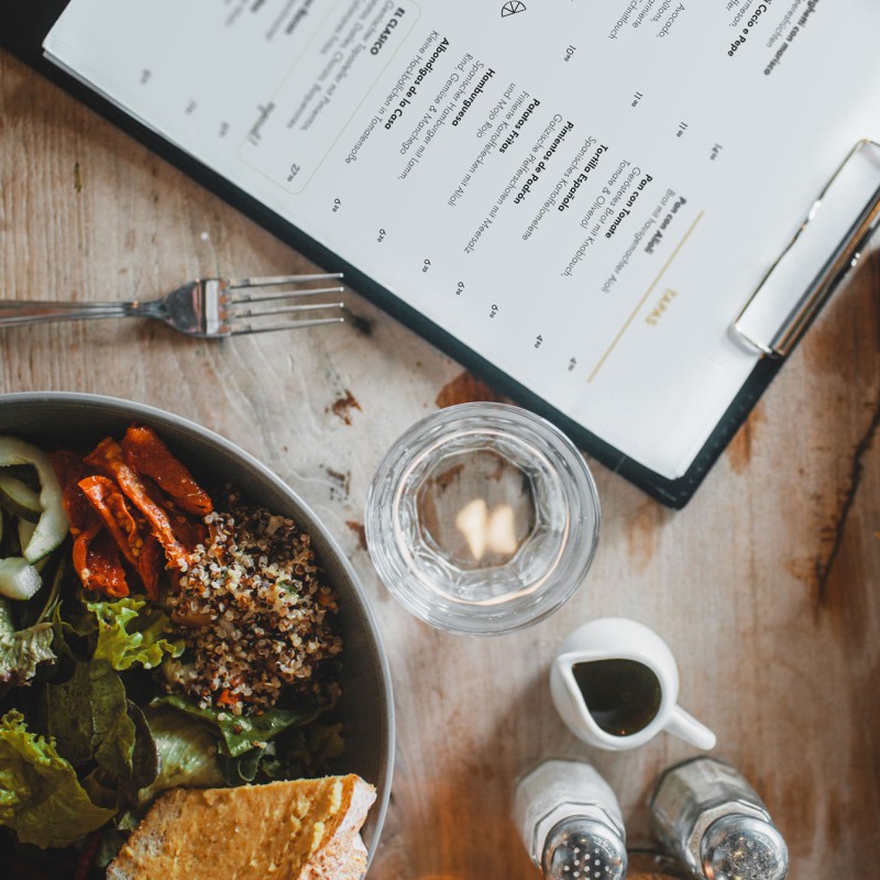An A4 menu on a clipboard lies on a table surrounded by plates of food.