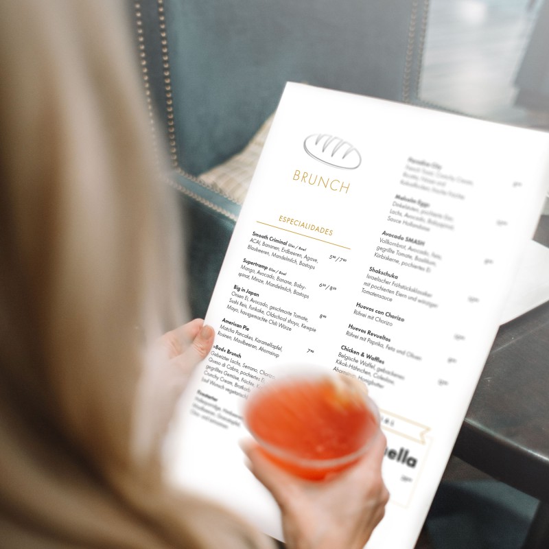 View over the shoulder of a woman holding a drink in her right hand and a menu in her left.