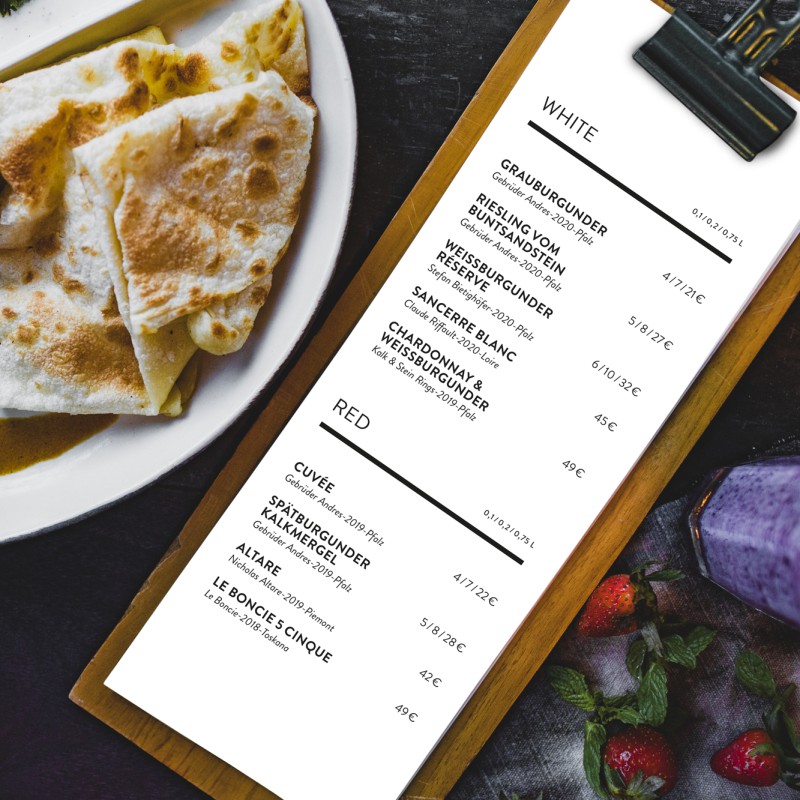 A small menu on a clipboard lies on a table surrounded by plates of food.